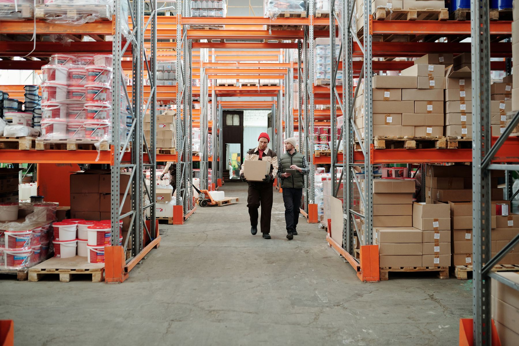 Two warehouse employees walking down an aisle with a carton and clipboard
